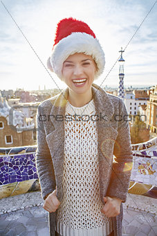 smiling trendy woman in Santa hat at Guell Park in Barcelona