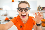 happy young woman in Halloween decorated kitchen taking selfie