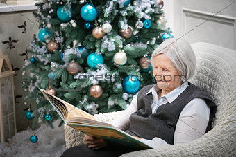 Senior woman reading a book beside a Christmas tree