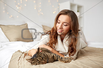 happy young woman with cat lying in bed at home