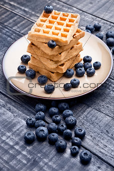 Blueberries and sweet waffles on plate and blue wood