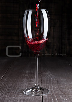 Pouring red wine from bottle to the glass on wood