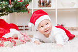 Cute baby in a Santa hat next to Christmas tree with presents