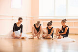 Young ballerinas putting on pointe shoes while sitting on floor in ballet class