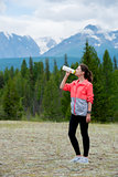 Beautiful woman runner drinking water outdoors. Mountains background.