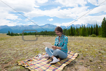Beautiful girl in a field on mountains, using  tablet pc.
