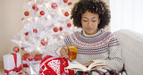 Woman reading a book in front of Christmas tree