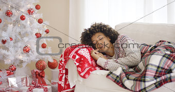 Woman sleeping on couch beside Christmas tree