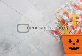 Halloween bucket with candies and jujube on gray concrete backgr