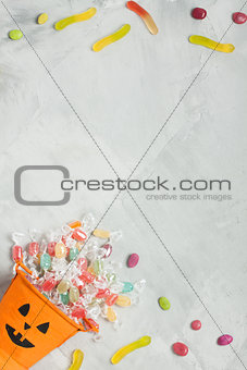 Halloween bucket with candies and jujube on gray concrete backgr