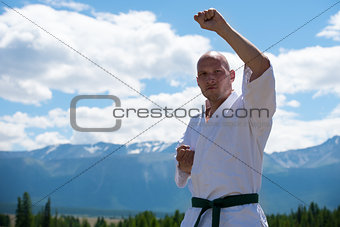 Man in white kimono and black belt training kung-fu, karate or aikido on mountain background.