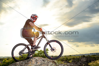Professional Down Hill Cyclist Resting with Bike on the Rock at Sunset. Extreme Sport.