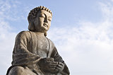 Sitting Buddha image in lotus position on sky background.