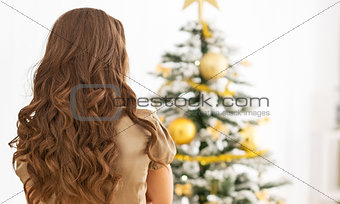 Young woman standing in front of christmas tree . rear view