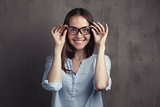 portrait of smiling woman with glasses near grey background wall