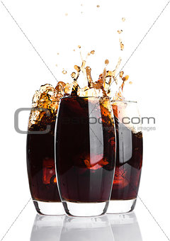 Glasses of cola with splash and ice cubes on white