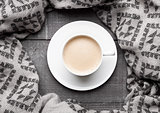 Cup of cappuccino with grey wool scarf on wood