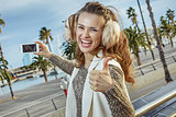 tourist woman showing thumbs up and taking photo with smartphone