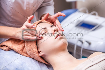 Young woman in spa salon, beautician performing facial massage