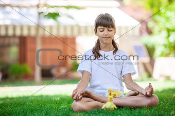 Little girl relaxing while sitting on grass, with small ducklings