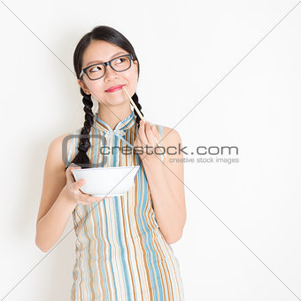 Oriental girl eating with chopsticks and thinking