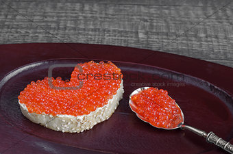 Sandwich with red caviar in the form of heart on a wooden tray. Analog products.