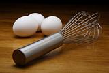 Three Eggs and a Whisk on a Wood Table