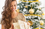 Happy young woman looking into shopping bag near christmas tree