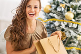 Happy young woman opening shopping bag near christmas tree