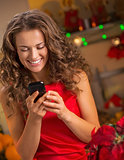 Happy young housewife writing sms in christmas decorated kitchen