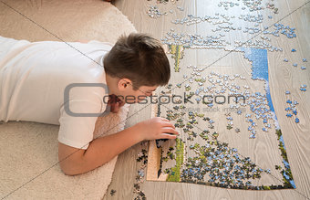 Teen boy collects a puzzle lying on carpet