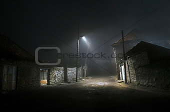 Night street country road with buildings and fences covered in fog lamp . Or Mysterious night in the centre of Ilisu village Gakh, Azerbaijan