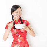 Oriental woman in red cheongsam eating with chopsticks