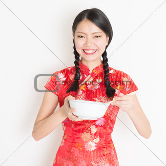 Oriental female in red cheongsam eating with chopsticks