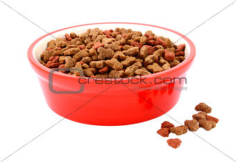 Dry cat food in a red bowl, biscuits spilled beside