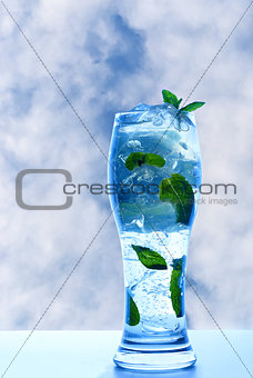 Mint drink with ice and leaves on sky background