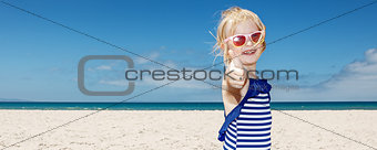 Girl in striped swimsuit on a white beach showing thumbs up