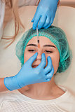 Woman receiving cosmetic injection through nose.