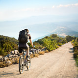 Man with Backpack Riding a Bicycle in Mountains