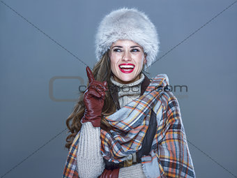 smiling elegant woman in fur hat isolated on cold blue got idea