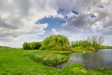 Spring landscape with lake, meadow, forest and sky with clouds