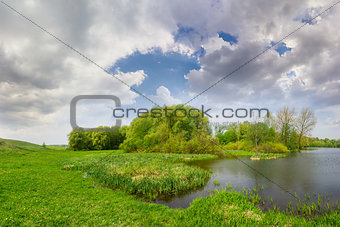 Spring landscape with lake, meadow, forest and sky with clouds