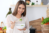 Young happy woman is cooking or eating fresh salad in the kitchen