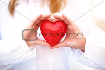 Young woman doctor holding a red heart, standing on gray background
