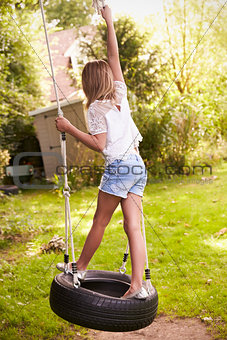 Rear View Of Young Girl Playing On Tire Swing In Garden