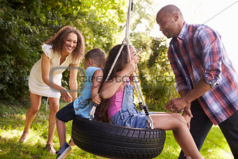 Parents Pushing Children On Tire Swing In Garden