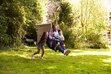 Daughter Pushing Father And Son On Tire Swing In Garden