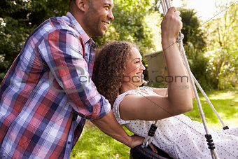 Side View Of Man Pushing Woman On Tire Swing In Garden