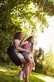 Mother And Daughter Sitting On Tire Swing In Garden