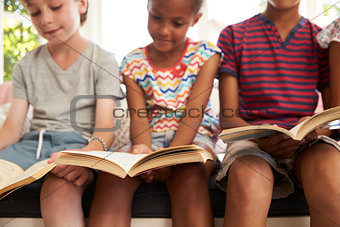 Close Up Of Children Reading On Window Seat